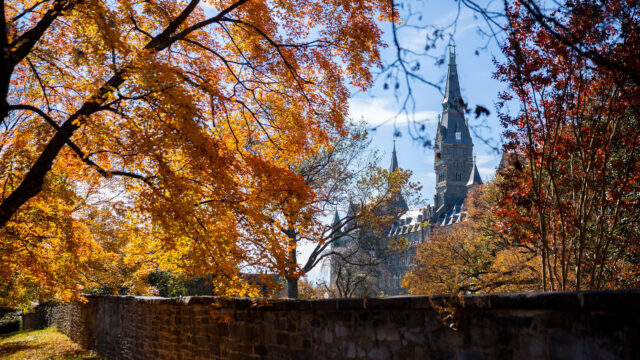 Photo of Front Gates in Fall with orange and brownish-red leaves- Healy Hall in background