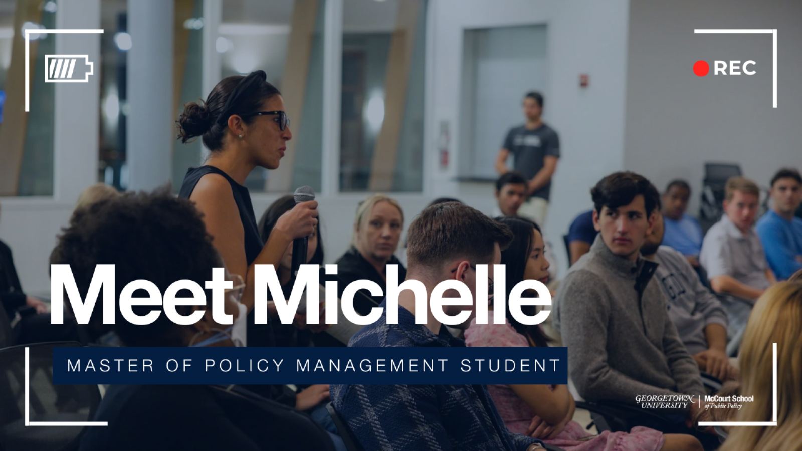 Student giving a speech in front of other Policy management students at Georgetown. The text overlay reads Meet Michelle,Master of Policy Management student