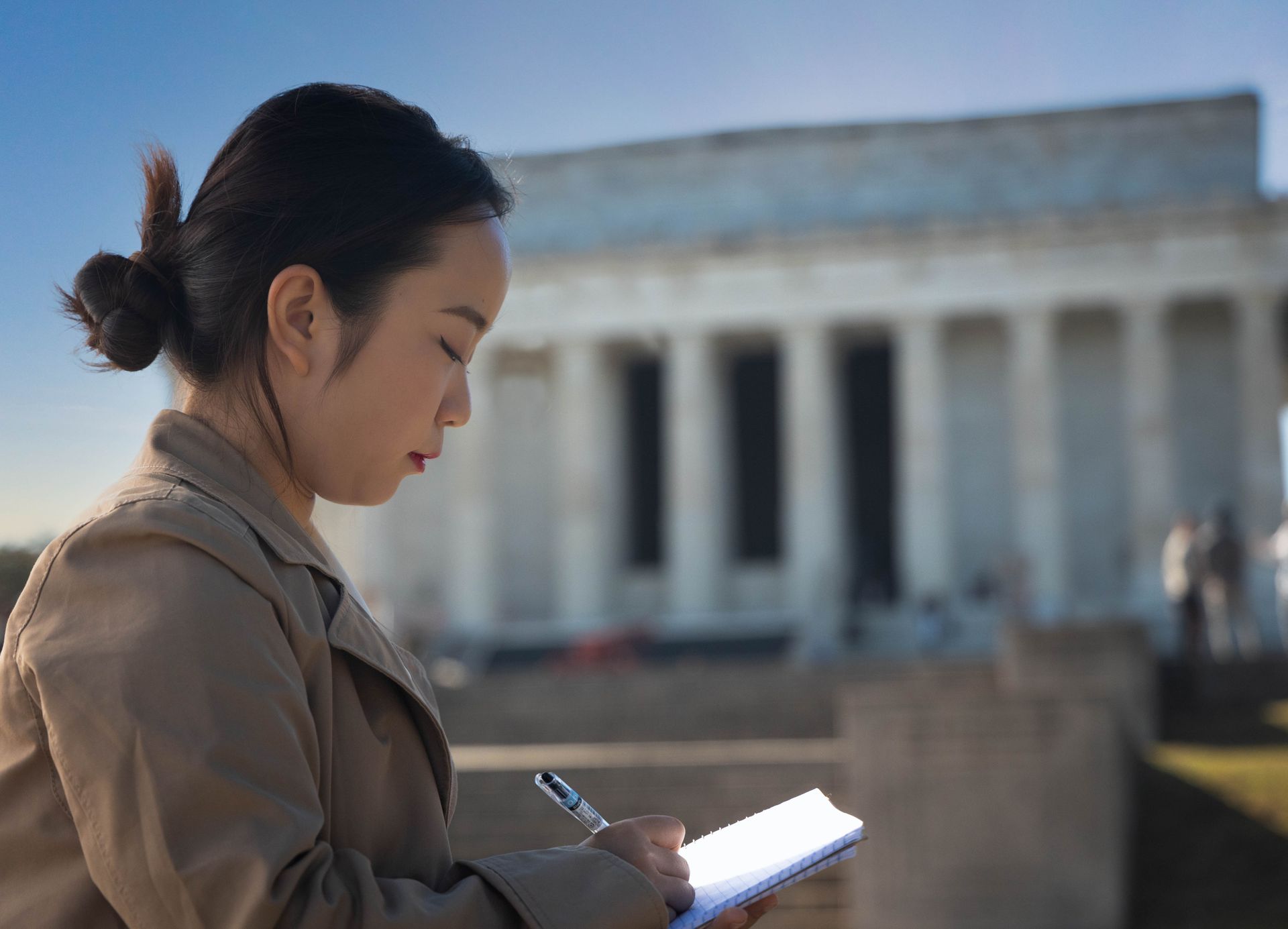 Woman writing in a notepad in front of the Lincoln Memorial