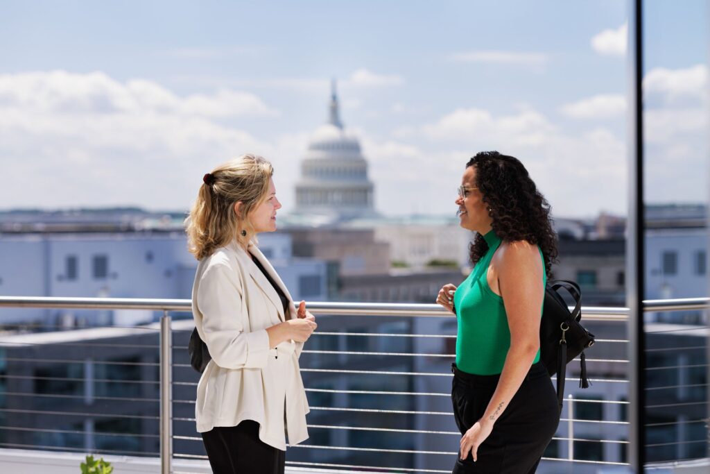 Two students talking on the roof of the new Capitol Campus building with the Capitol Building in the distance.