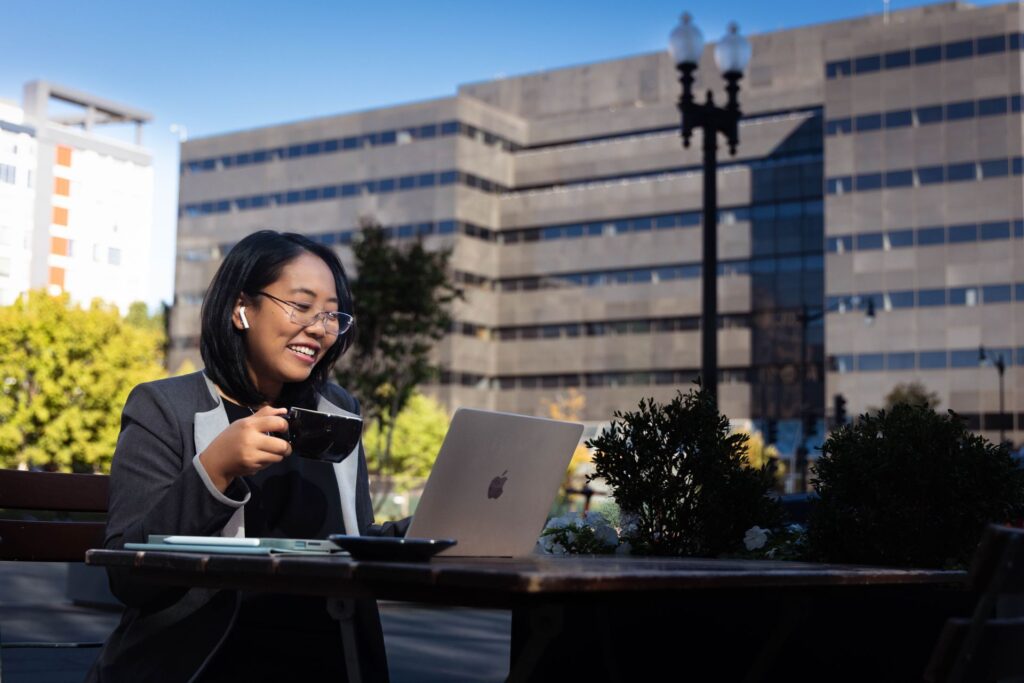 A student working at a laptop outside with a cup of coffee.