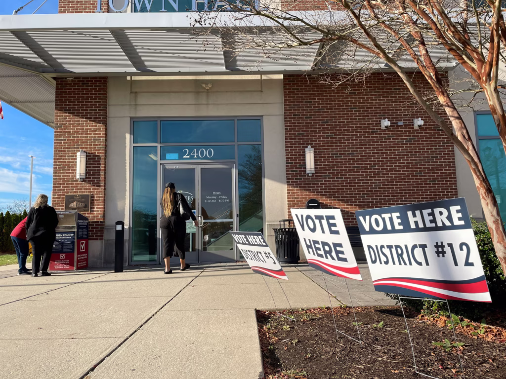 People walking into county election building, vote-here signs in the foreground