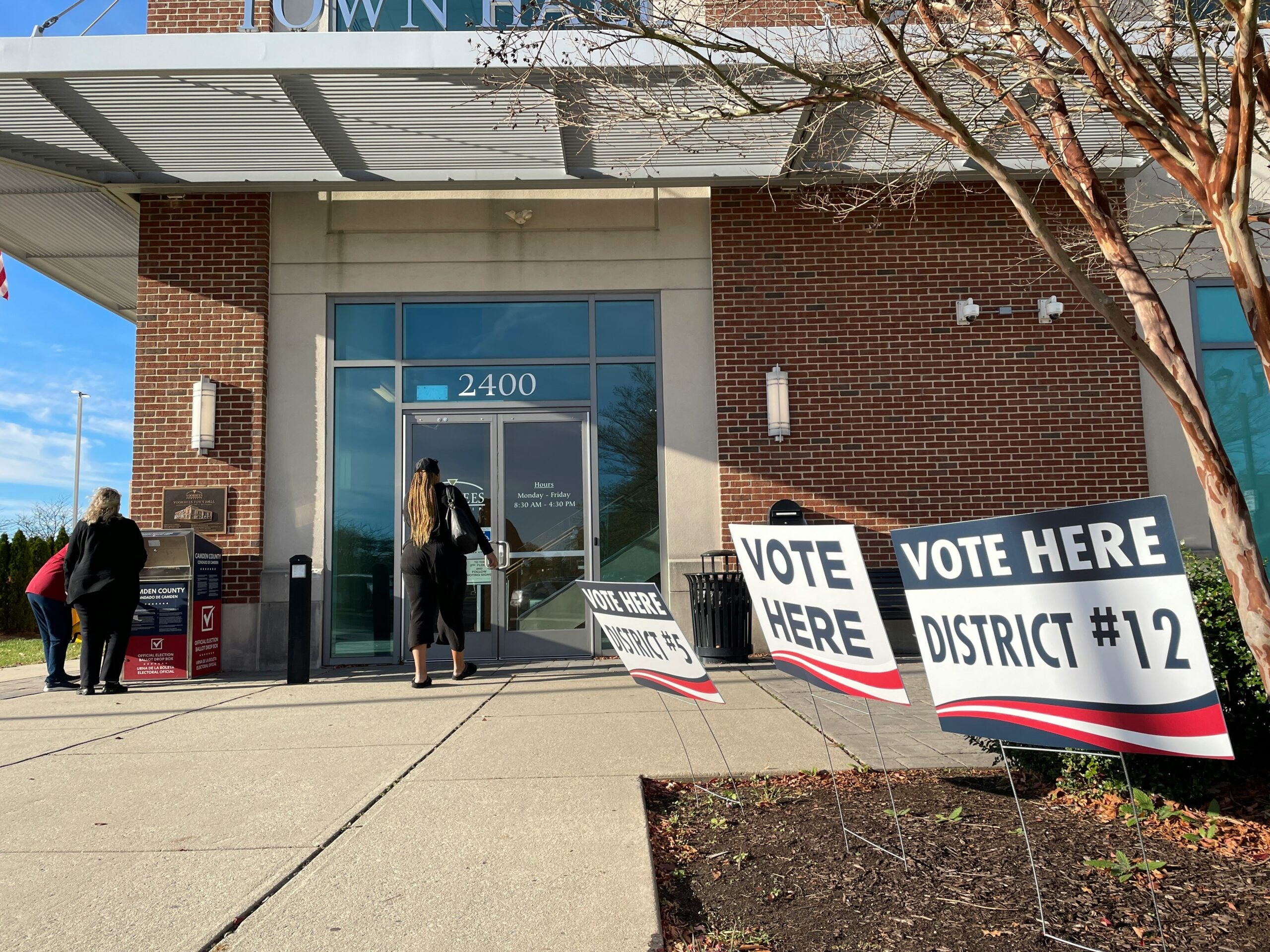 Woman enters a polling location inside a mall to cast a ballot in the November 8, 2022 midterm election while two other women examine a ballot drop box.