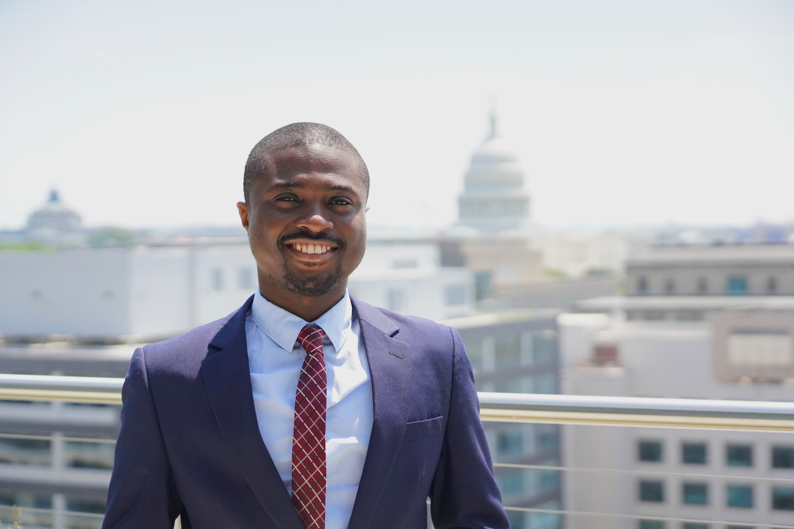 Nicholas Mensah stands on the rooftop of the McCourt School, US Capitol in the distance