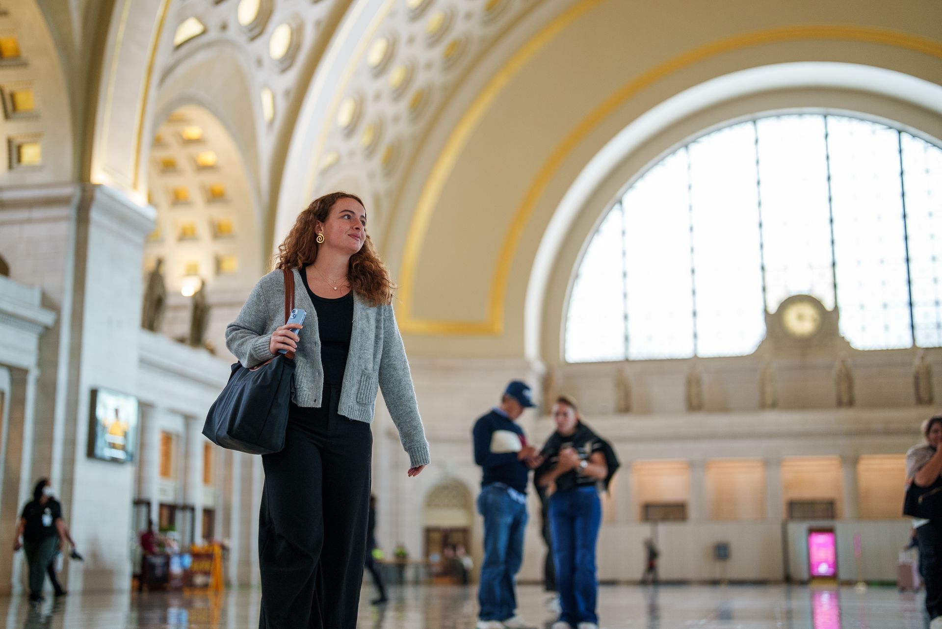 A student walking through Union Station in Washington, DC. holding a cell phone and smiling.