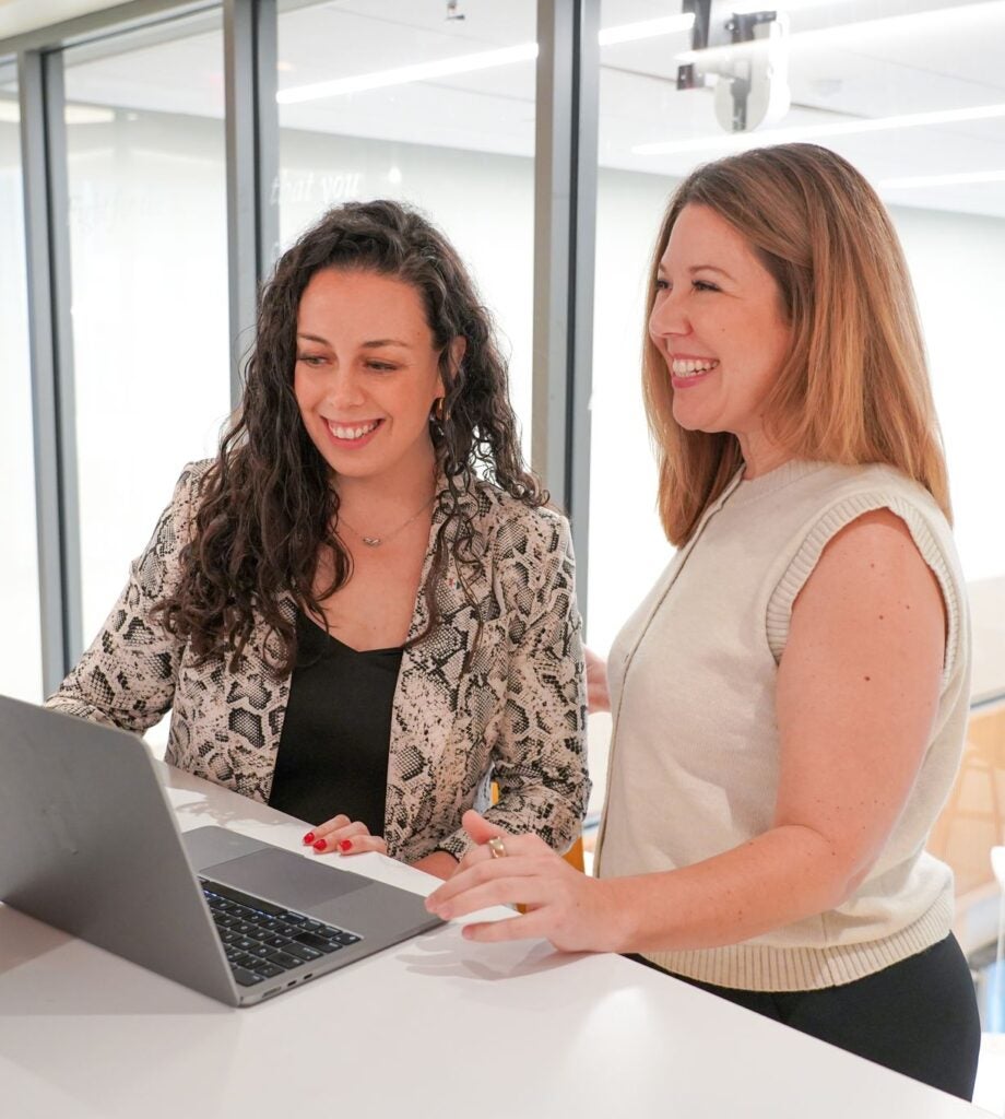 Two students smiling and looking at a laptop.