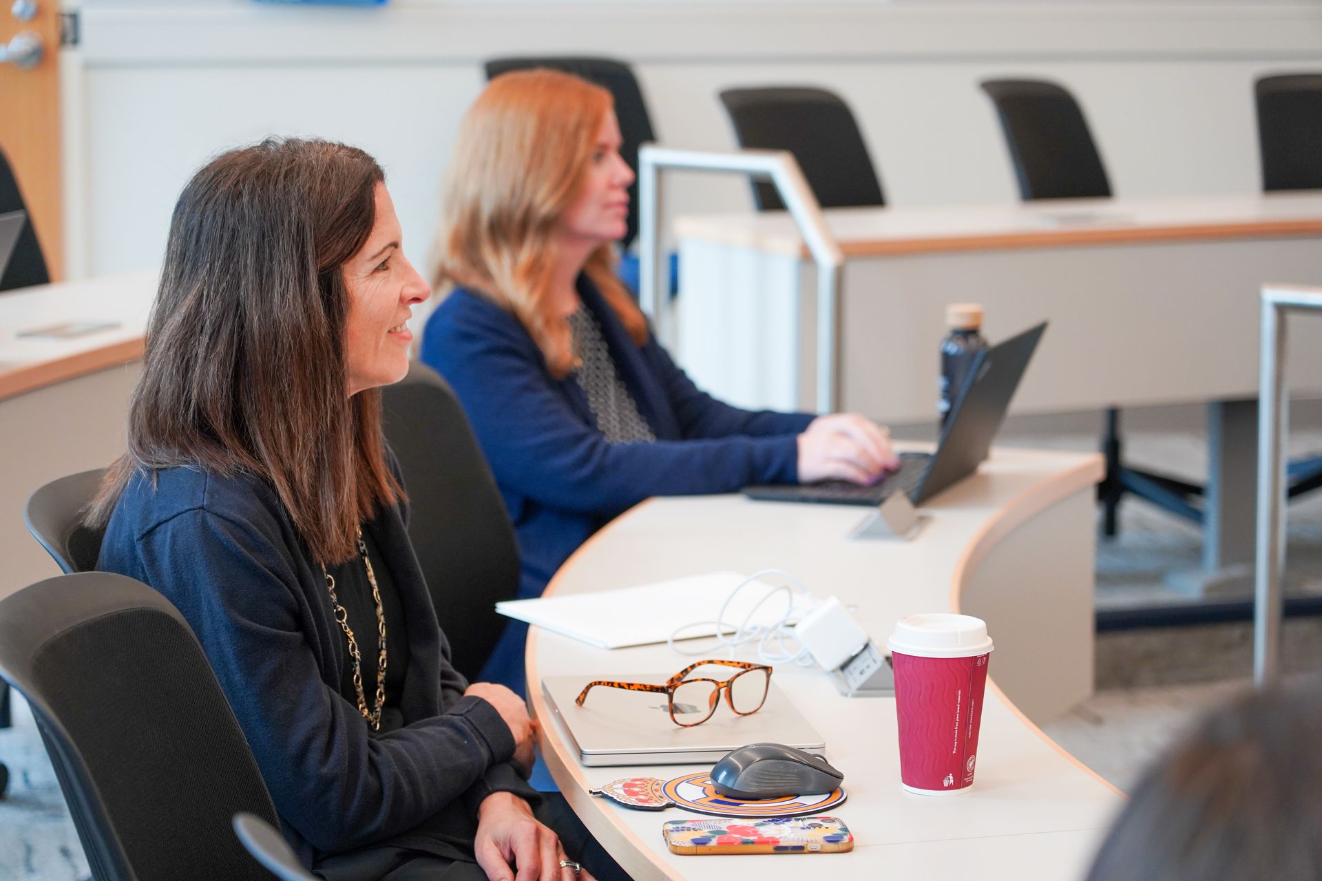 Two students listening intently in class. One is taking notes.