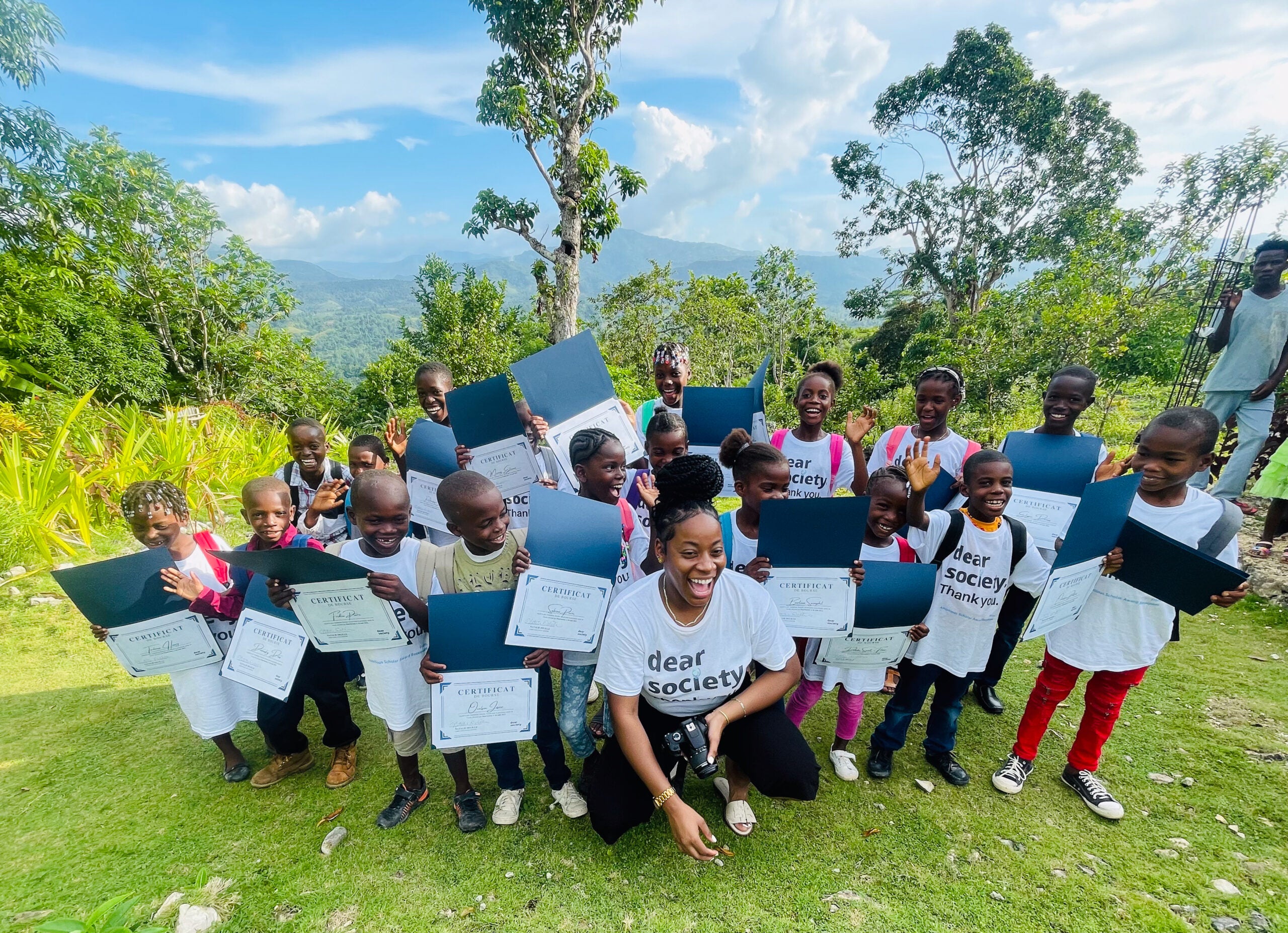 Natalie Delille kneeling with a large group of students outside in lush green area of Haiti