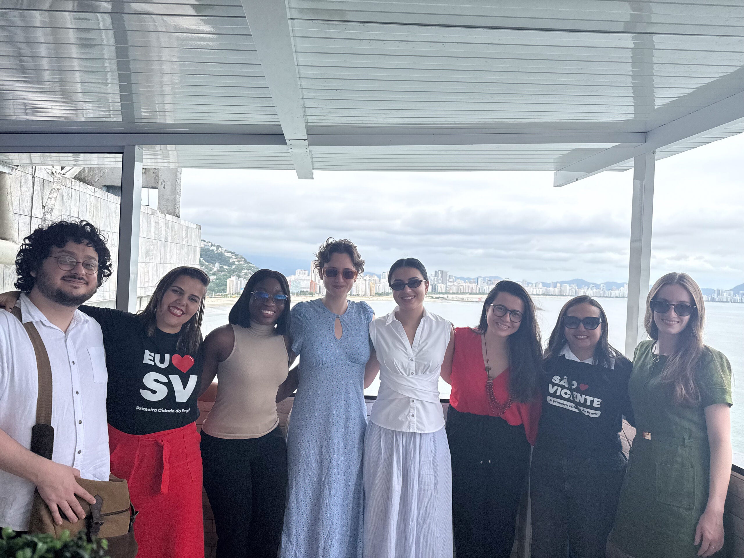 Eight individuals stand side-by-side in front of body of water