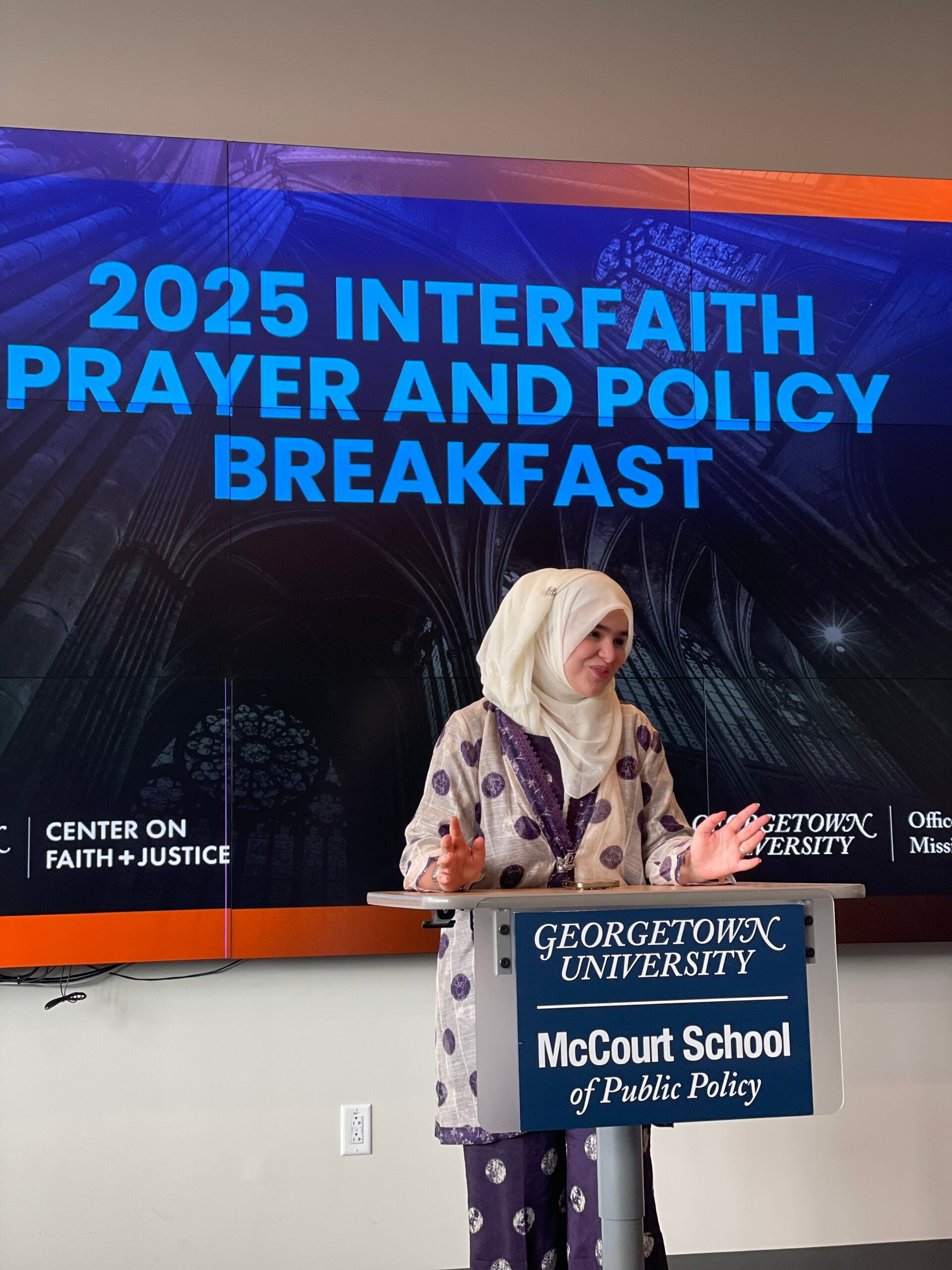 Bashir stands at podium leading interfaith prayer