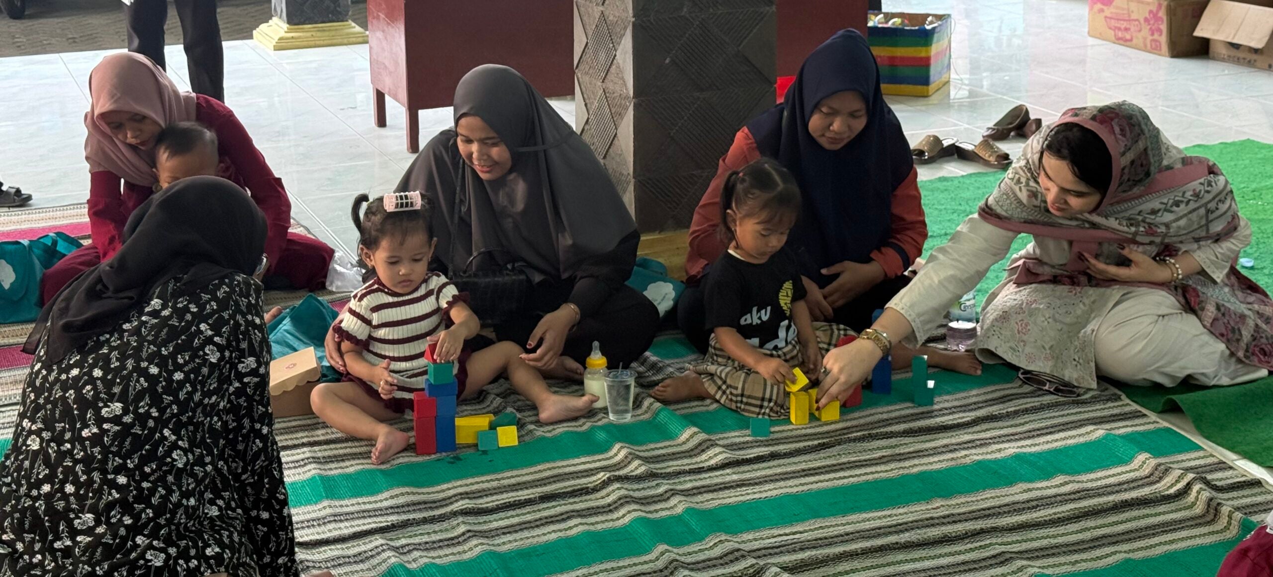 Women seated on the ground playing with young children