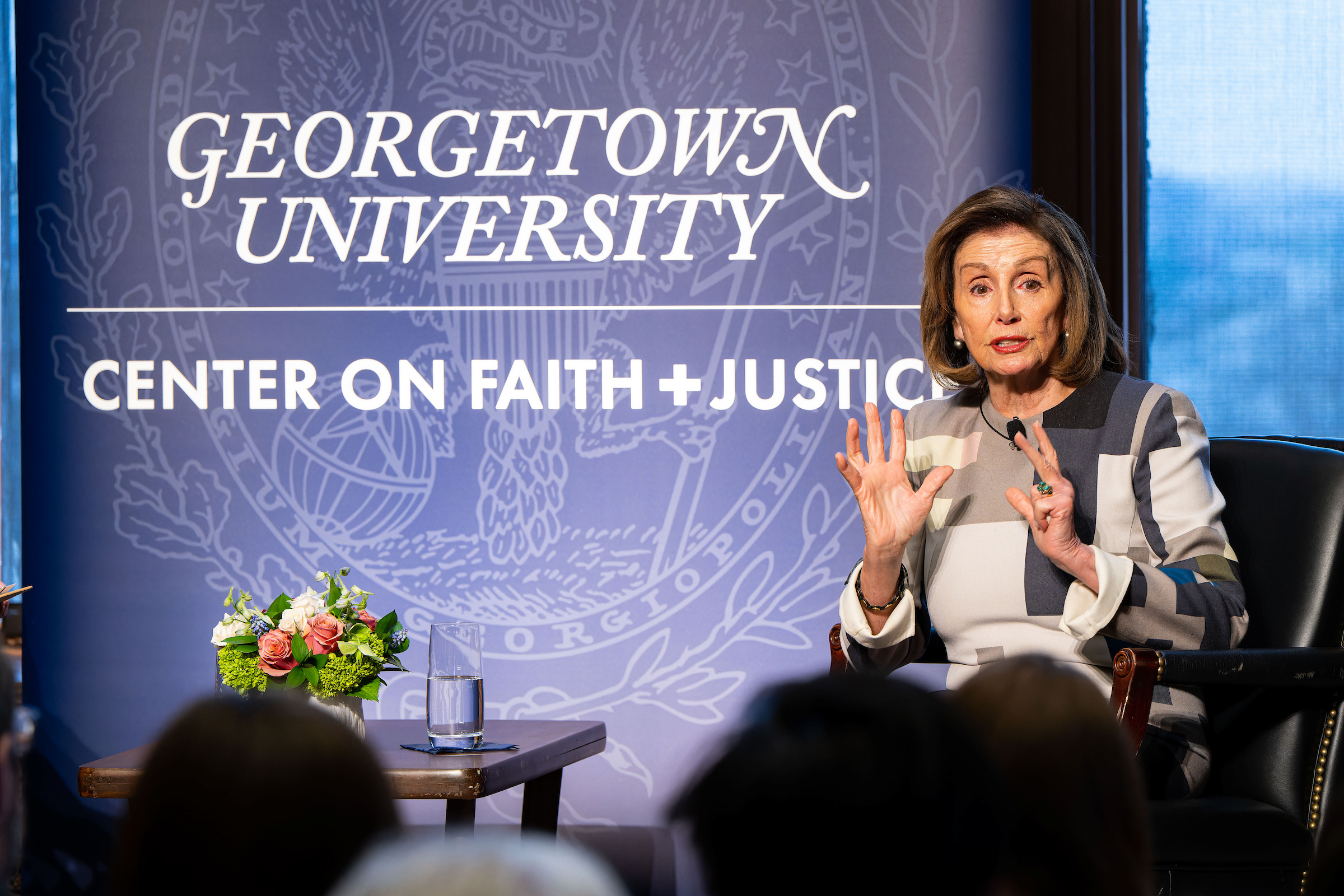 An older woman speaking, hands are raised and open. Background is banner that read "center on faith and justice"