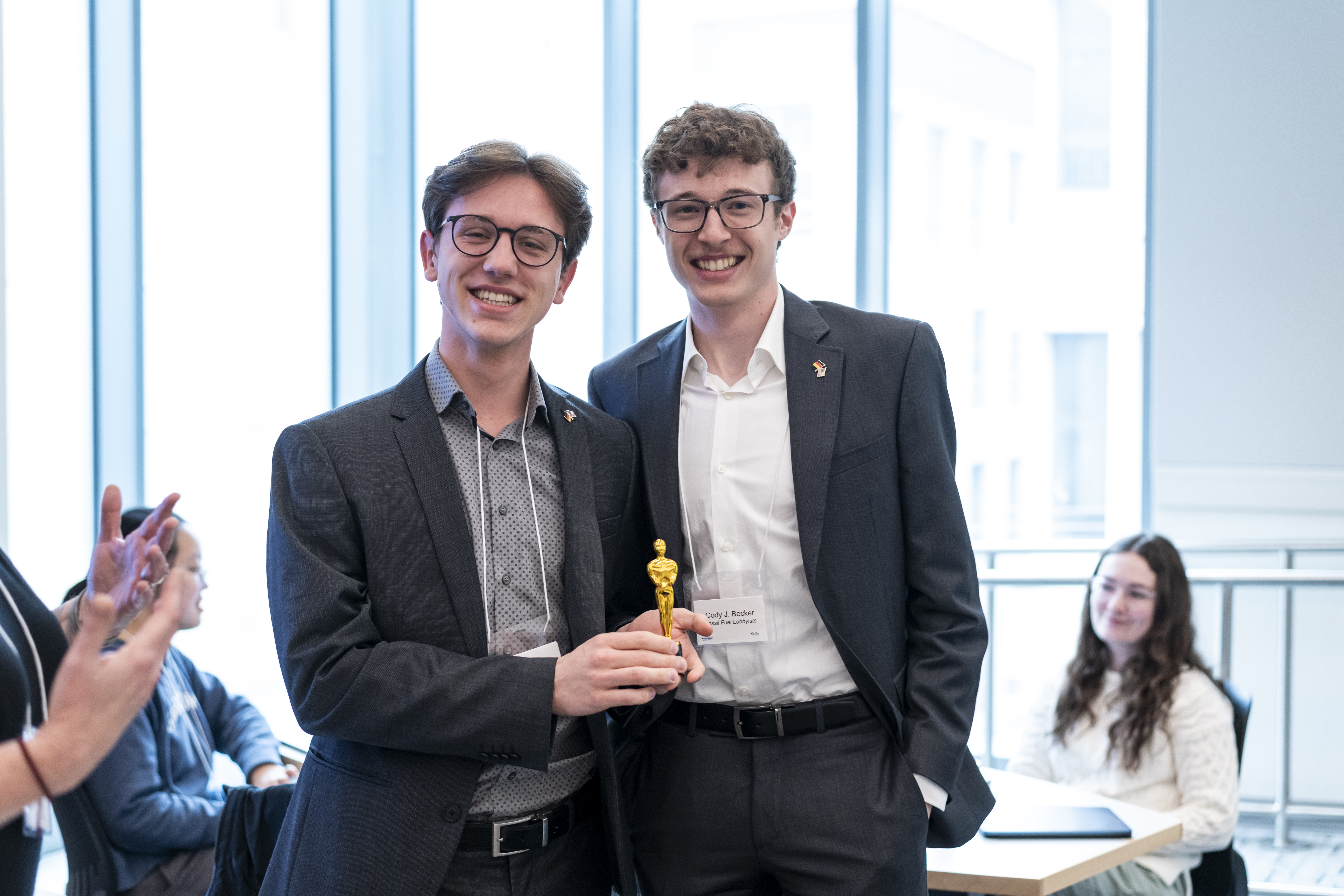 Two students standing side-by-side, one holds small golden trophy