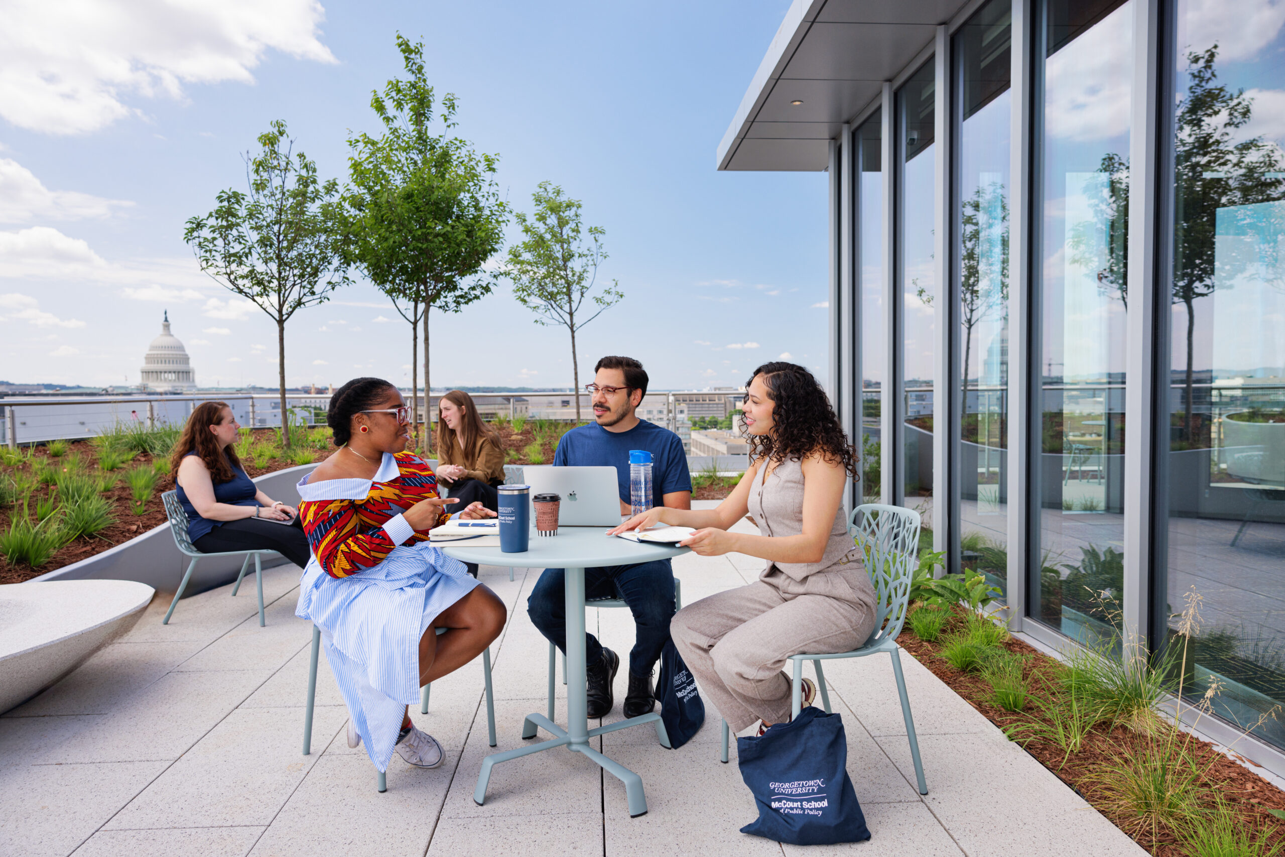 Three students sitting on McCourt rooftop, US Capitol in the background