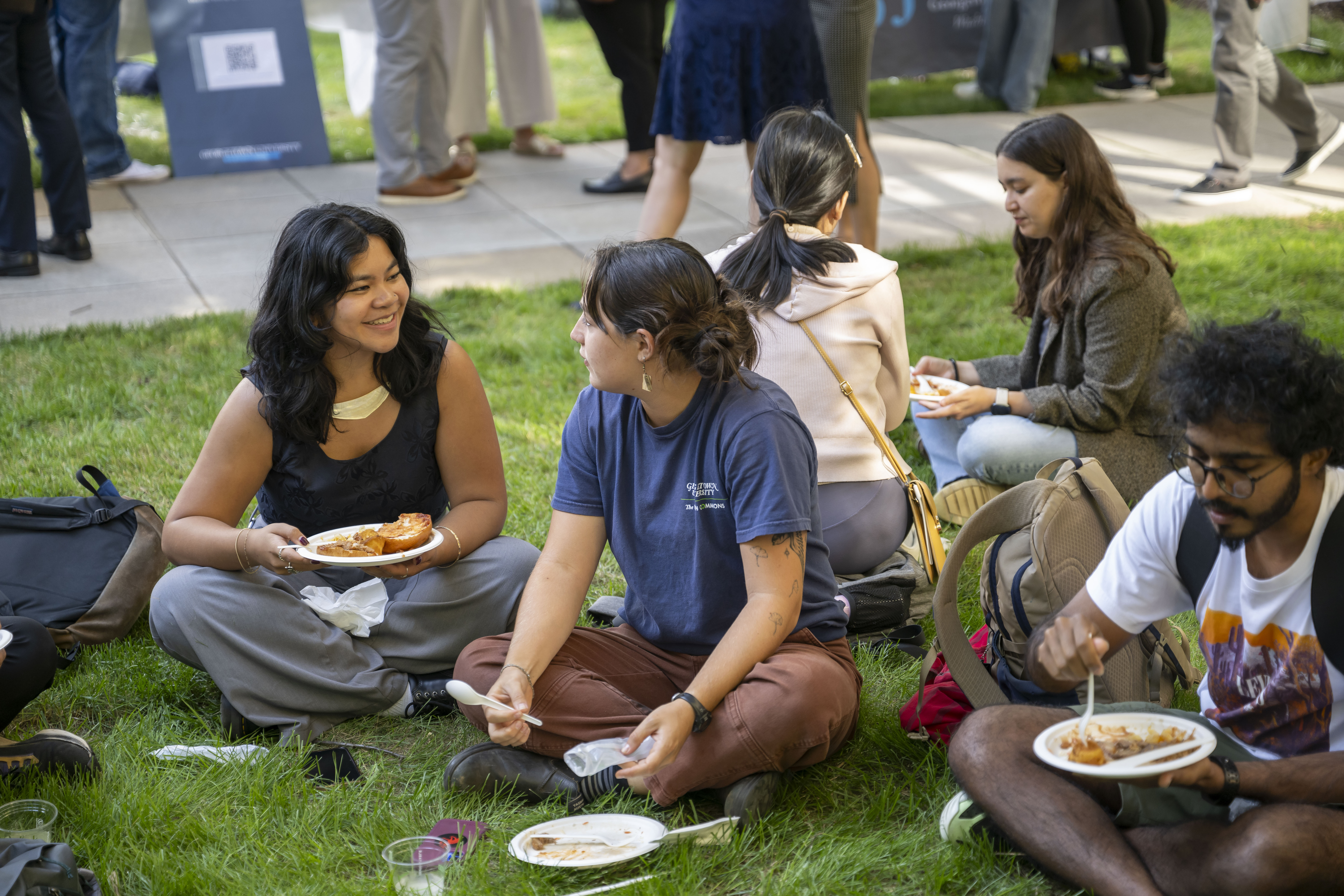 A group of students sitting in grass lawn, eating from paper plates