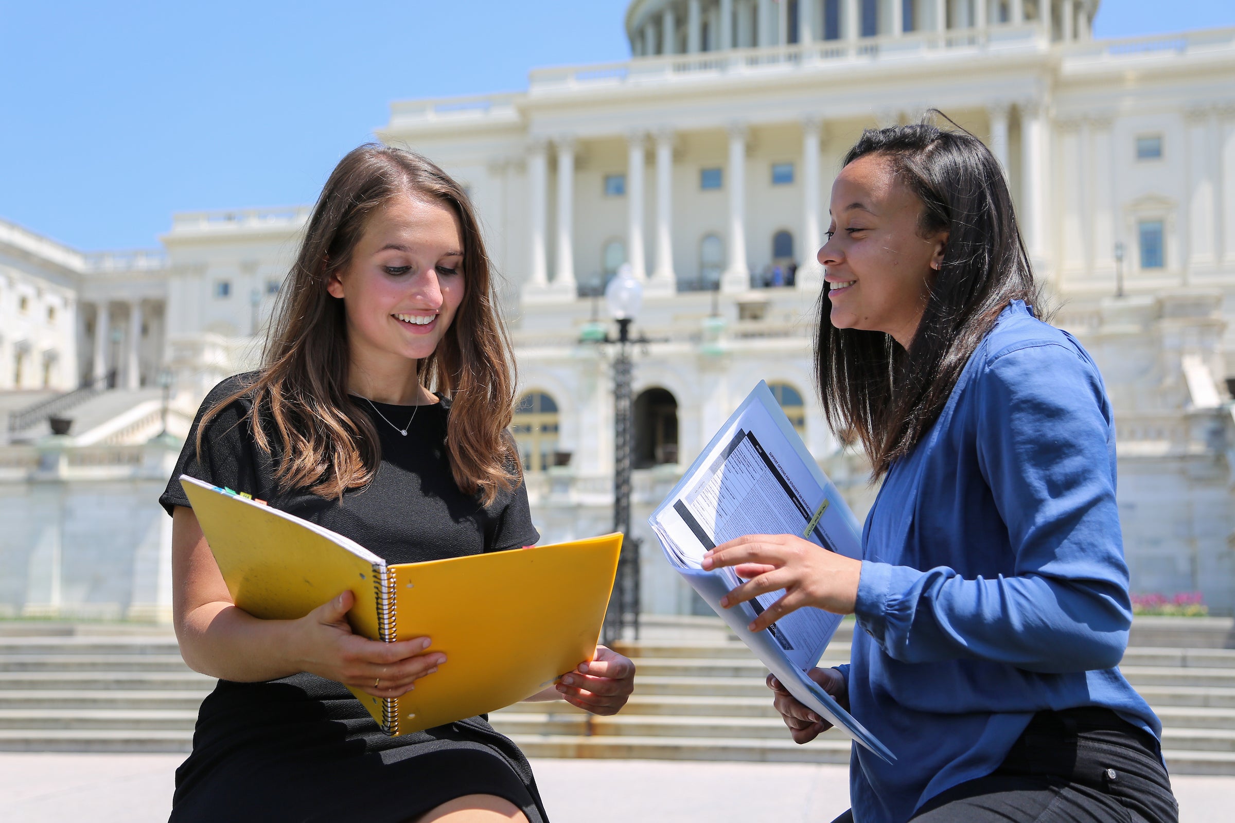 Two women comparing folders in front of the US Capitol