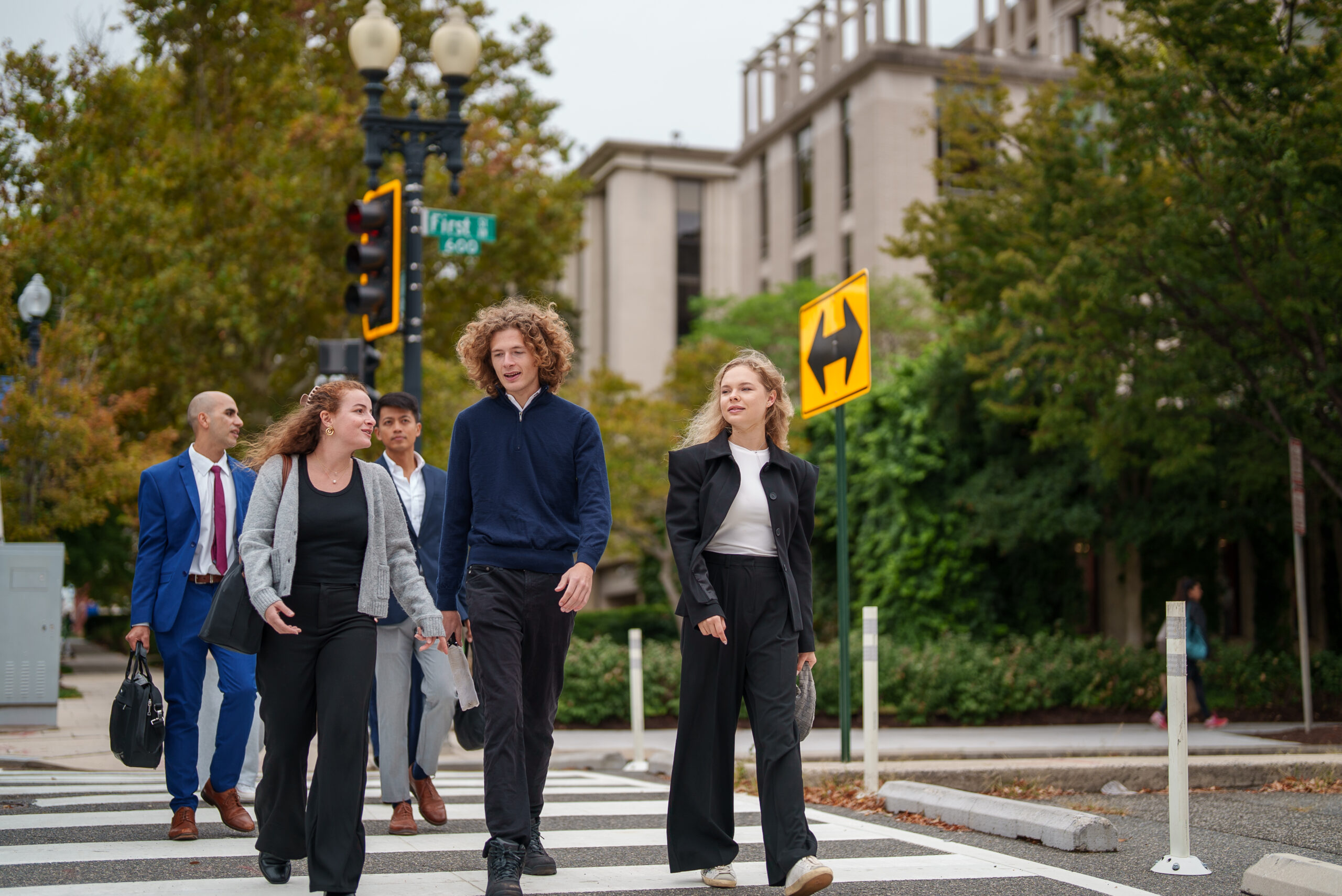 Five professionally-dressed people walking across a downtown DC street, two carrying briefcases