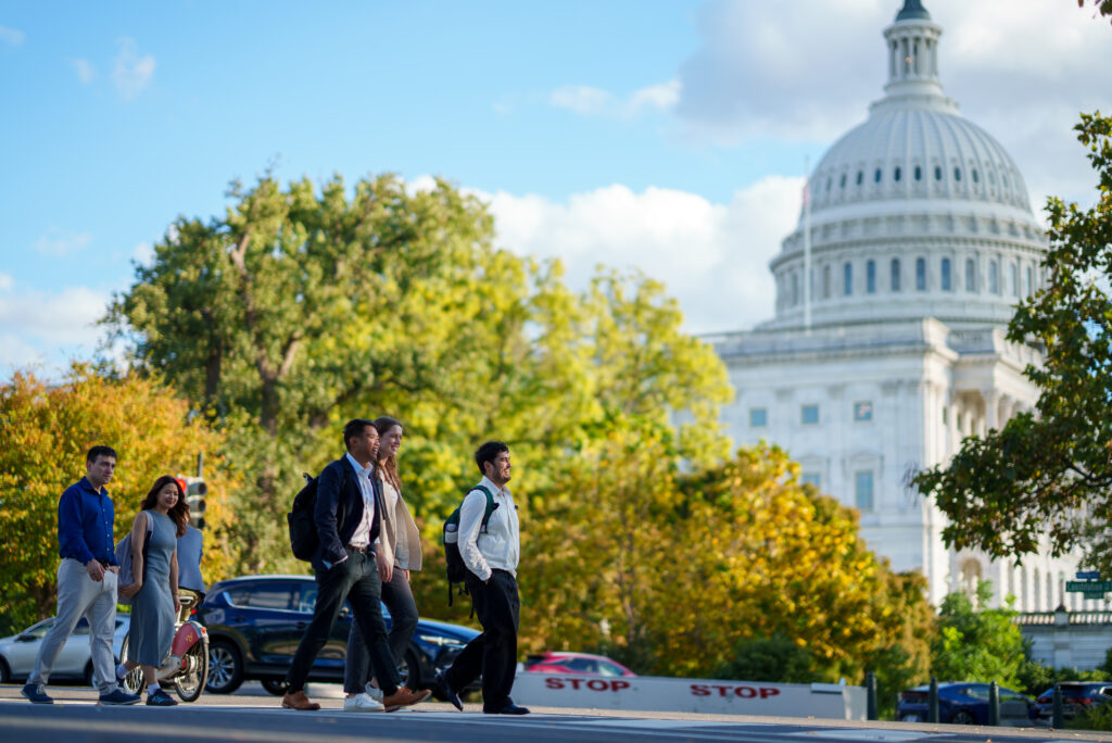 A group of people walking across the road, US Capitol in the background