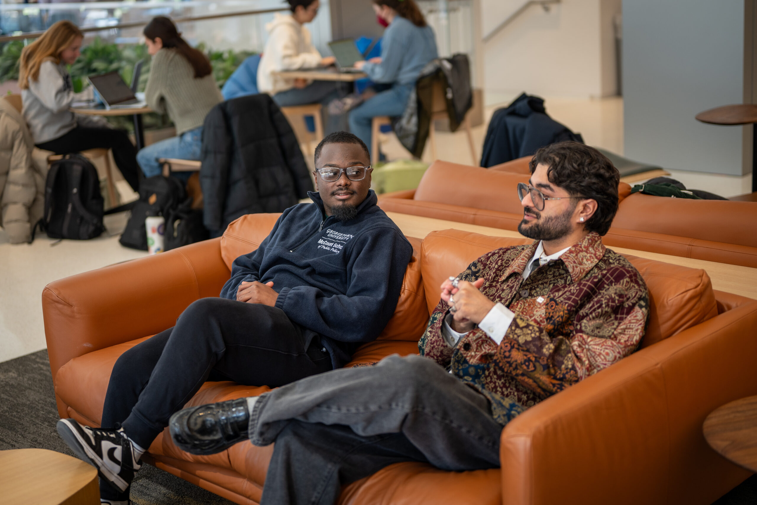 Two young men sitting and talking on rust-orange sofa