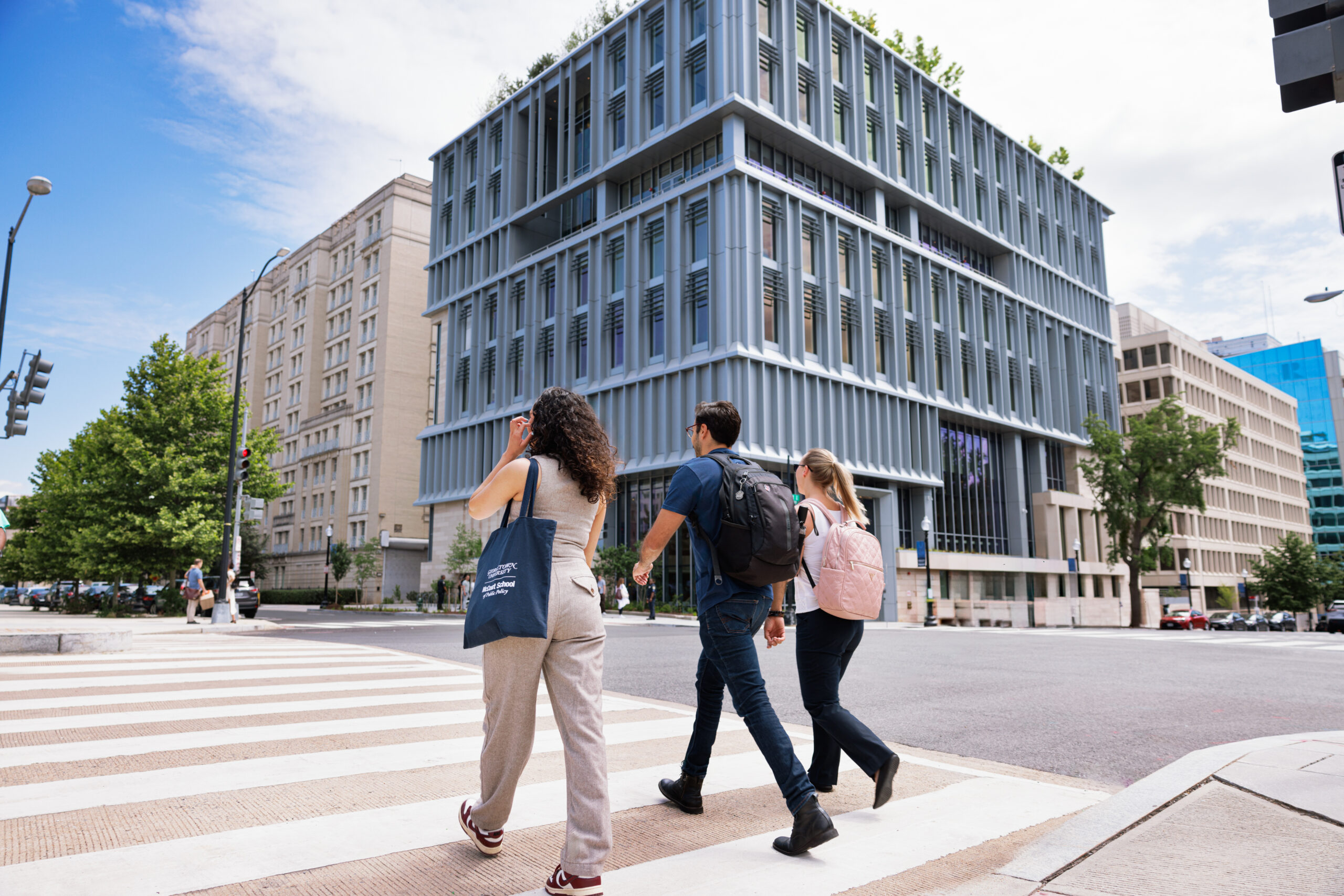 Three people walking across the street, McCourt's 125 E building in the background