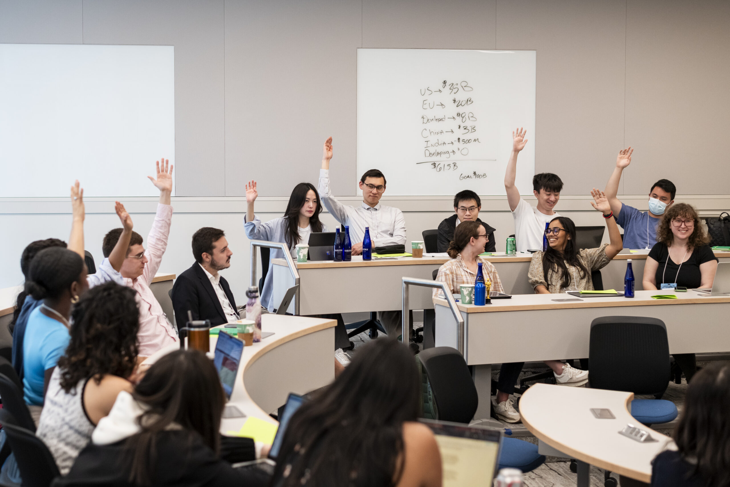 Large group of people raising hands in brightly-lit classroom