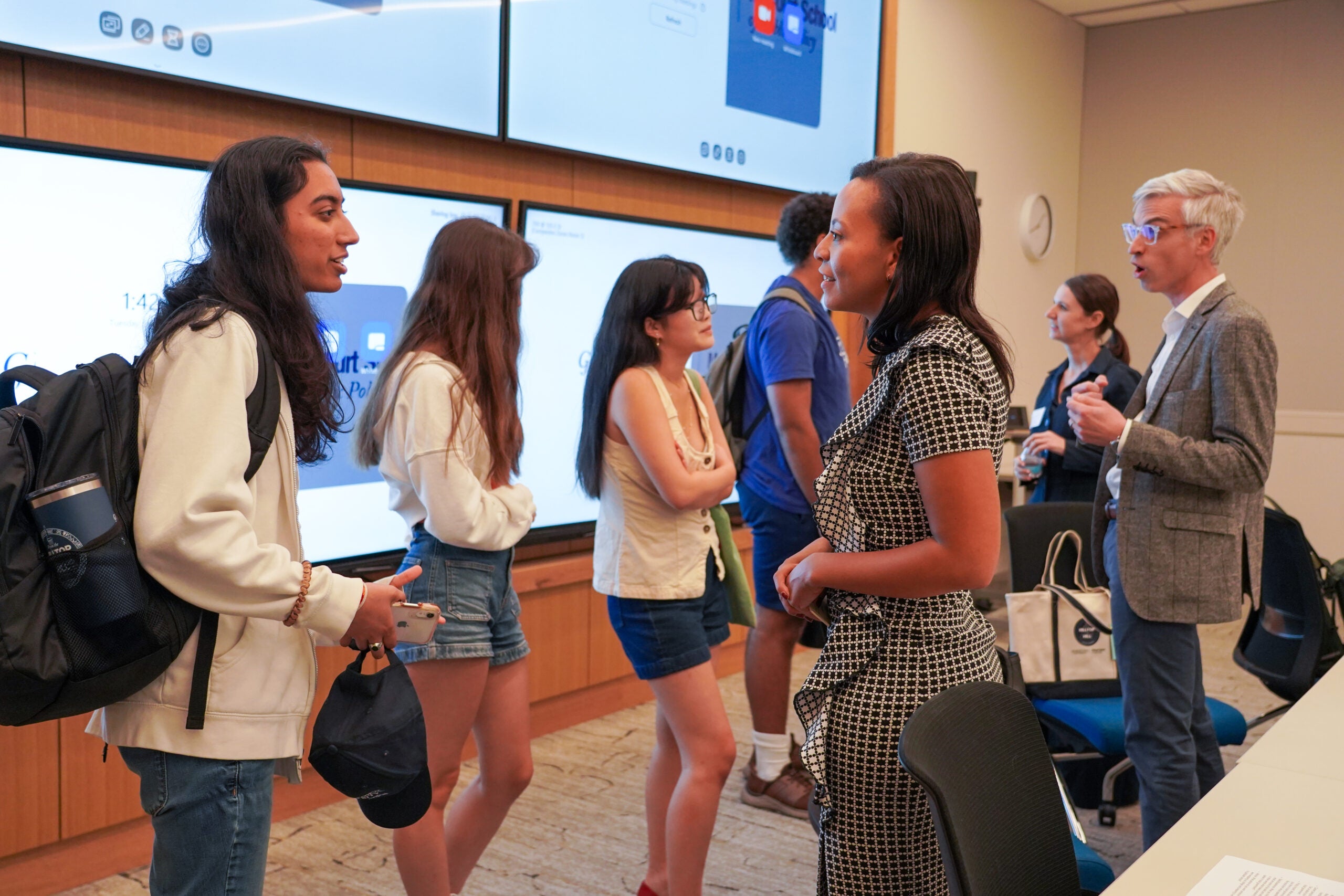 Multiple people standing and talking; a student speaks directly to presenter in foreground.
