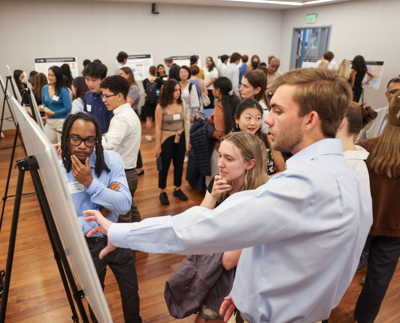 Multiple people looking at scientific poster, one man pointing at poster directly