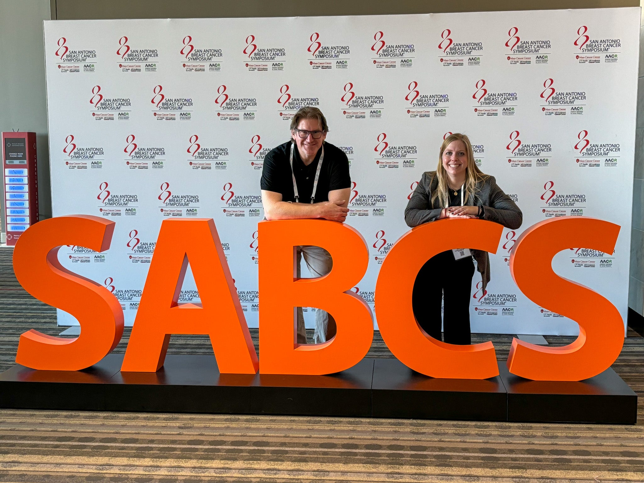 Two individuals leaning against giant letters that spell out "SABCS"