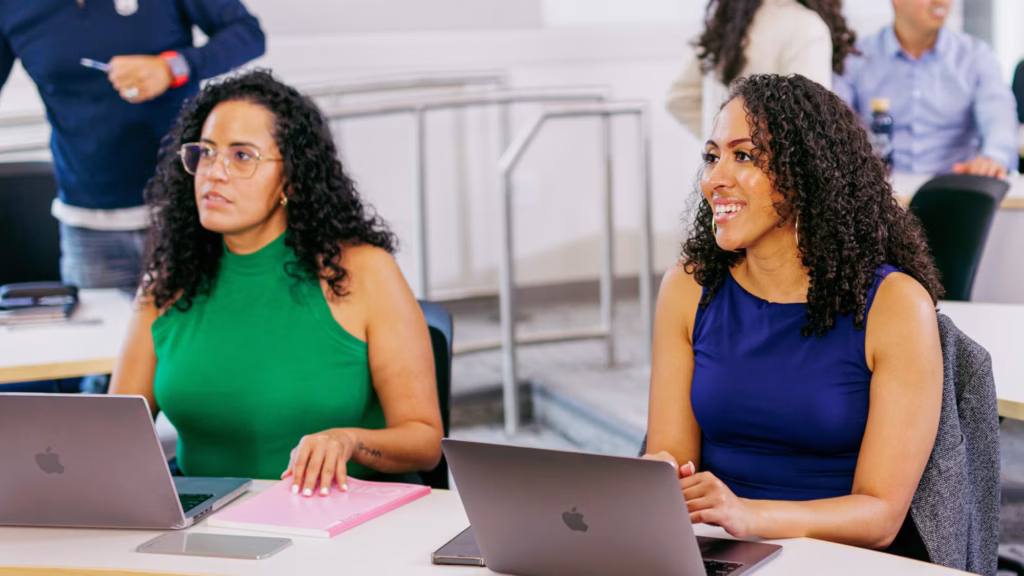 Two students at a desk with laptops.