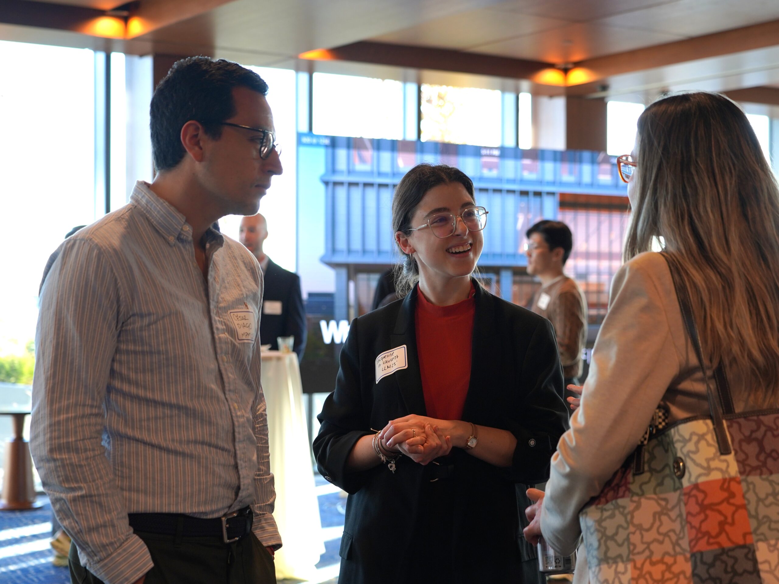 Three people standing nearby, speaking; dressed professionally.