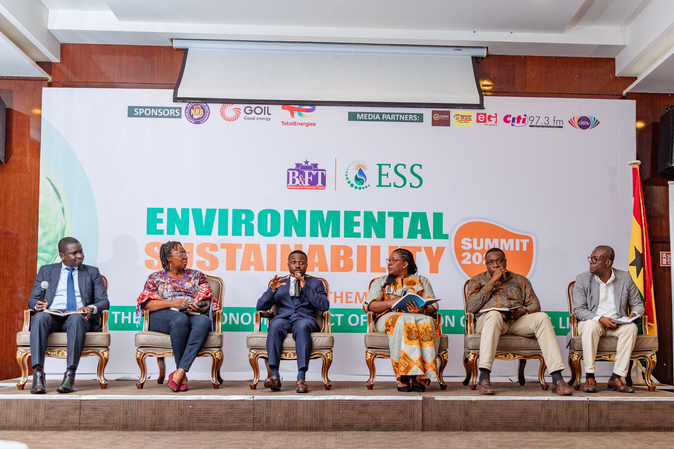 Nicholas Mensah, sits amongst five others on large stage, holding microphone and speaking on environmental sustainability