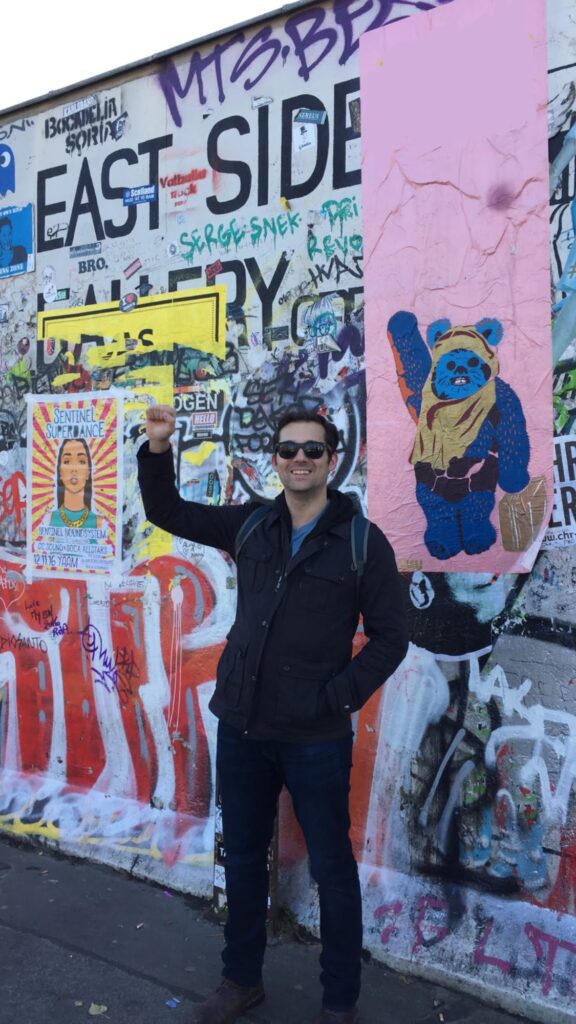 Colin McCollester standing before the Berlin Wall