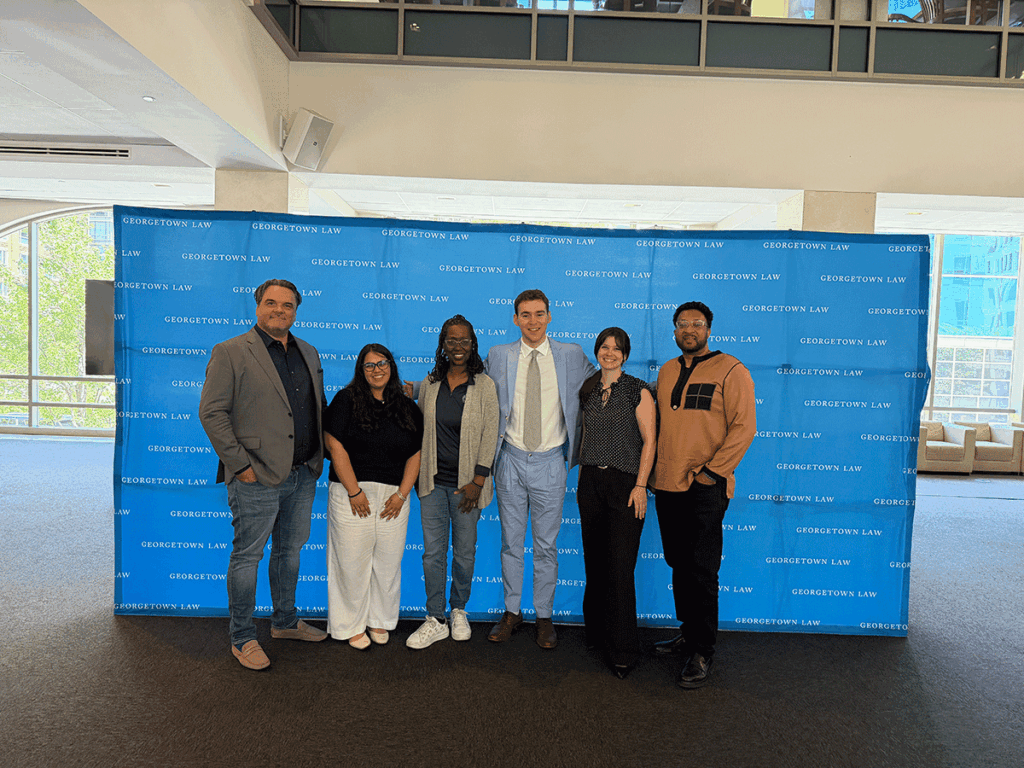 Six individuals standing in front of blue banner that reads "Georgetown Law"
