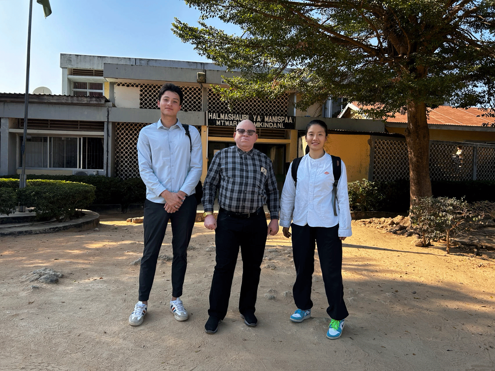 Three people standing out front of Tanzania education office